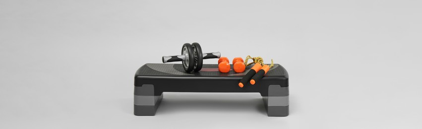 Image of Step platform, skipping rope, dumbbells and abdominal wheel on light background, space for text. Banner design