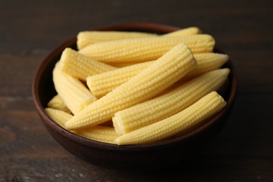 Photo of Tasty fresh yellow baby corns in bowl on wooden table