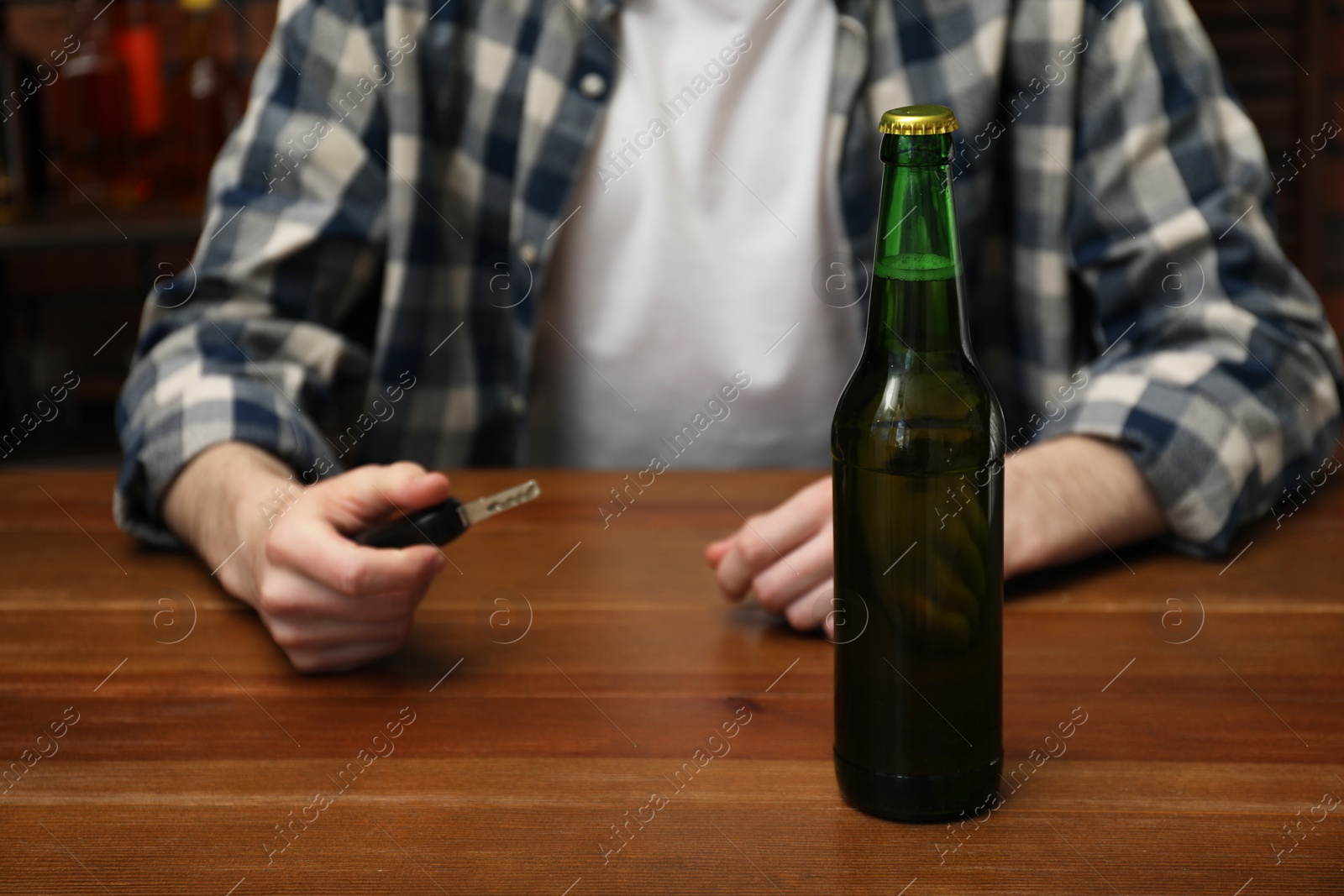 Photo of Man with car keys at table with bottle of beer, closeup. Don't drink and drive concept