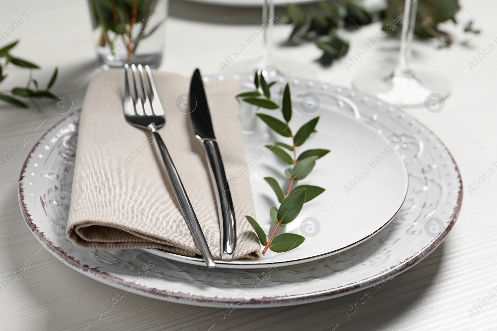 Photo of Stylish setting with cutlery and eucalyptus leaves on white wooden table, closeup