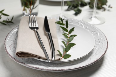 Stylish setting with cutlery and eucalyptus leaves on white wooden table, closeup