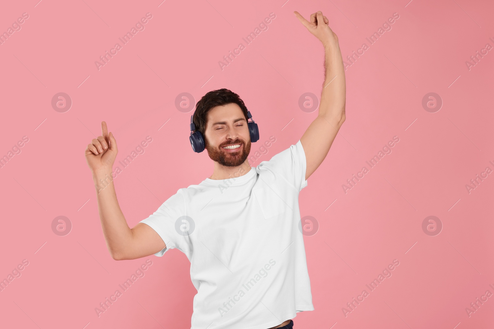 Photo of Happy man listening music with headphones on pink background