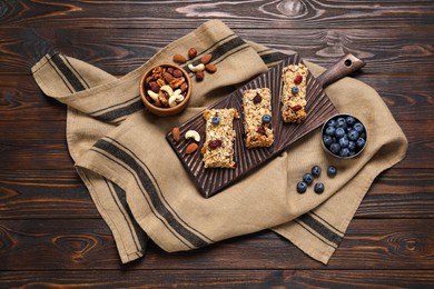 Tasty granola bars and ingredients on wooden table, flat lay