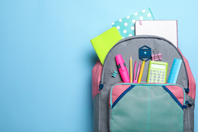 Photo of Stylish backpack with different school stationery on light blue background, top view. Space for text
