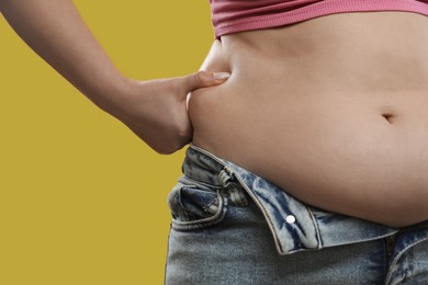 Woman touching belly fat on yellow background, closeup. Overweight problem