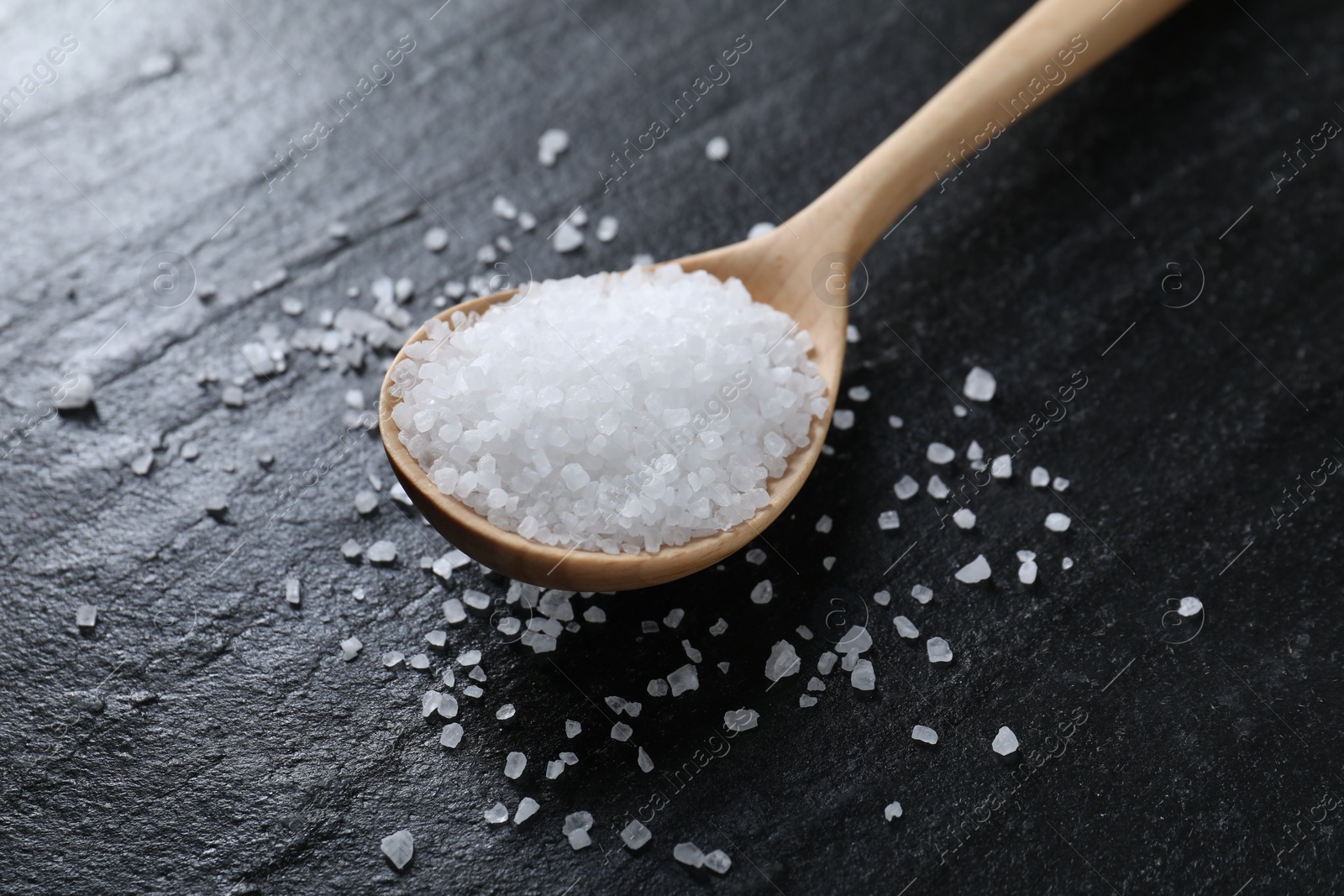 Photo of Organic white salt and spoon on black table, closeup