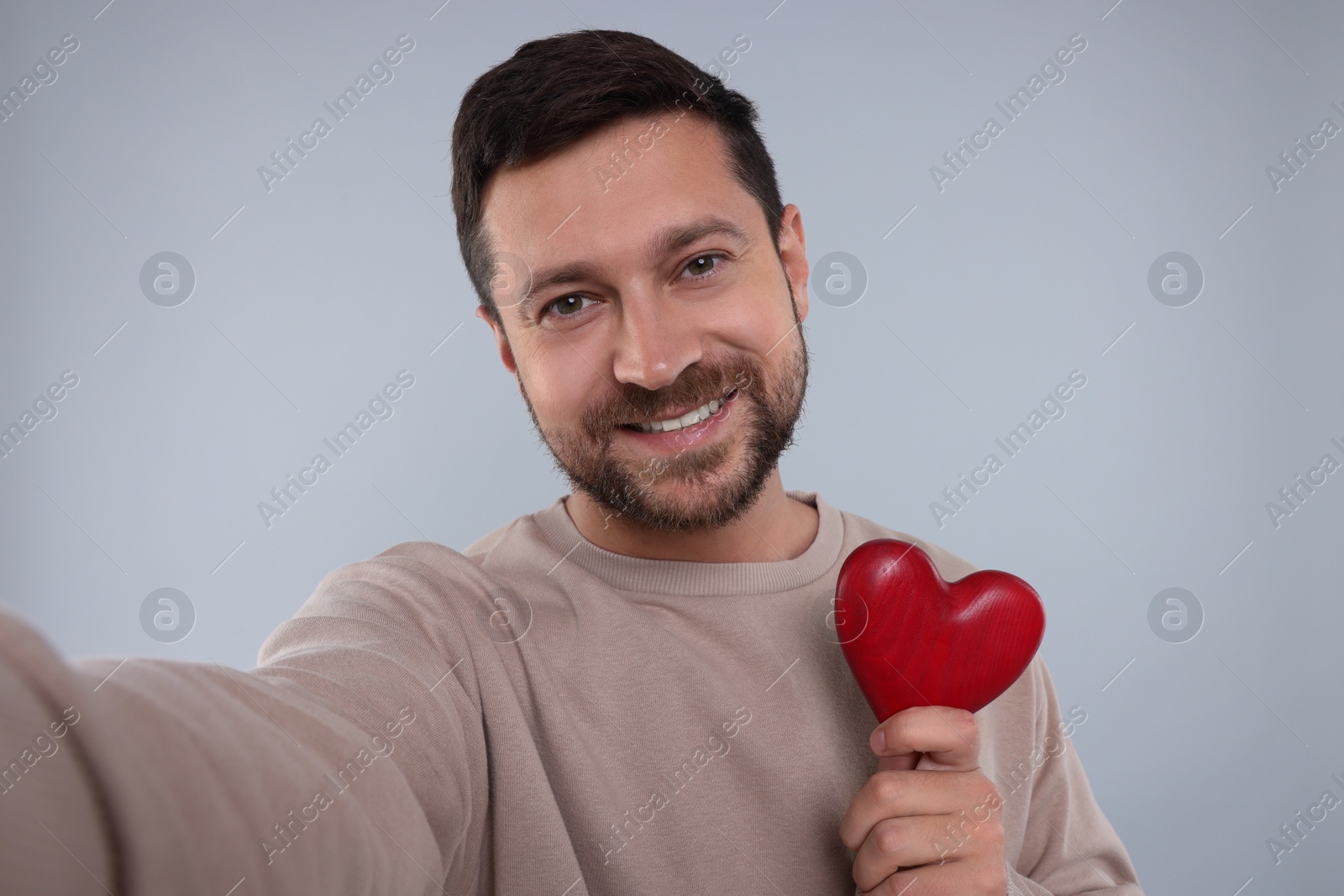Photo of Happy man holding red heart and taking selfie on light grey background