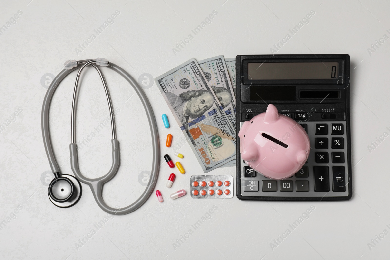 Photo of Piggy bank, stethoscope, calculator, money and pills on white textured table, flat lay. Medical insurance