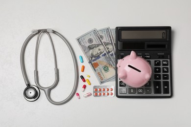 Photo of Piggy bank, stethoscope, calculator, money and pills on white textured table, flat lay. Medical insurance