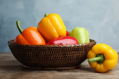 Photo of Wicker bowl with ripe bell peppers on wooden table against light blue background