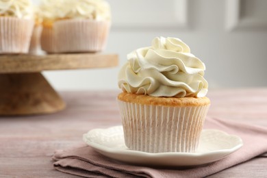 Photo of Tasty cupcake with vanilla cream on pink wooden table, closeup