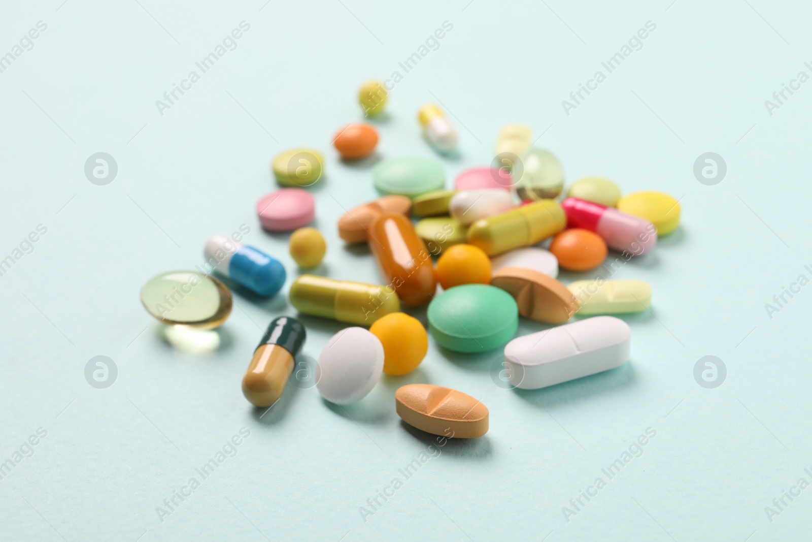 Photo of Many different pills on light blue background, closeup