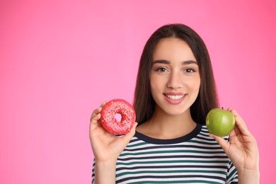 Photo of Woman choosing between apple and doughnut on pink background