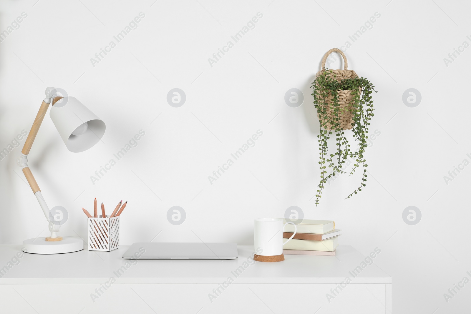 Photo of Cozy workspace with laptop, lamp and stationery on white desk at home