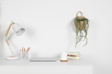 Cozy workspace with laptop, lamp and stationery on white desk at home