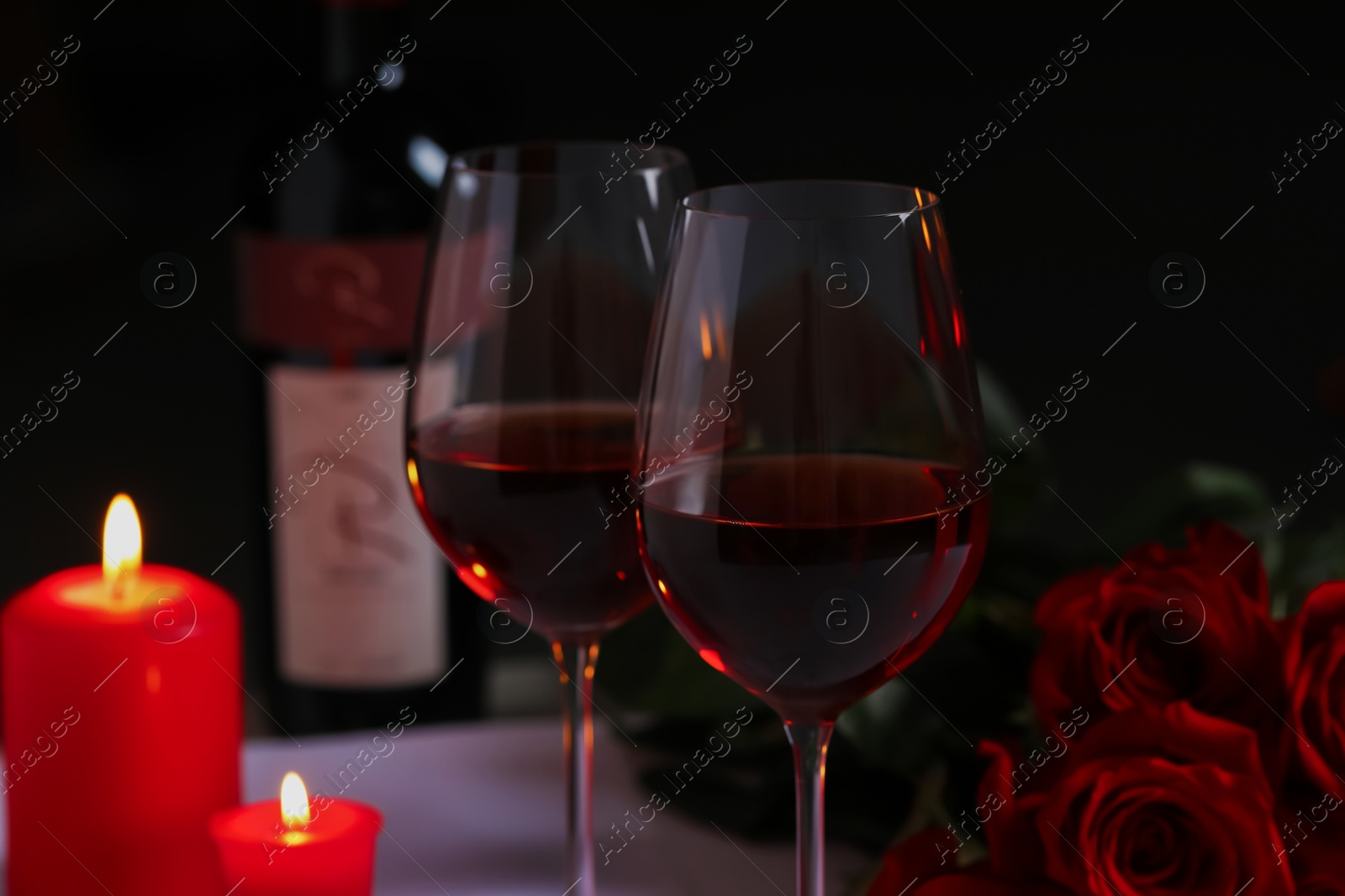 Photo of Romantic table setting with glasses of red wine, rose flowers and burning candles