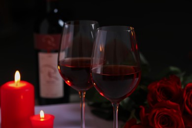Romantic table setting with glasses of red wine, rose flowers and burning candles