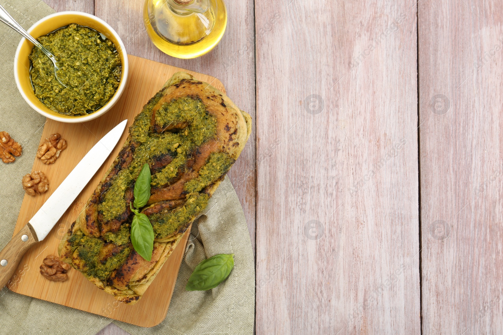 Photo of Freshly baked pesto bread with basil and knife on wooden table, flat lay. Space for text