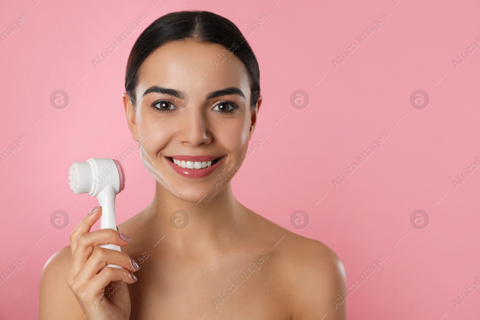 Photo of Young woman holding facial cleansing brush on pink background, space for text. Washing accessory