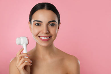 Young woman holding facial cleansing brush on pink background, space for text. Washing accessory