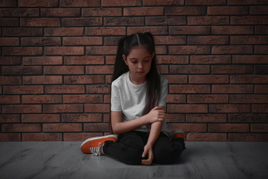 Photo of Sad little girl on floor near brick wall. Child in danger