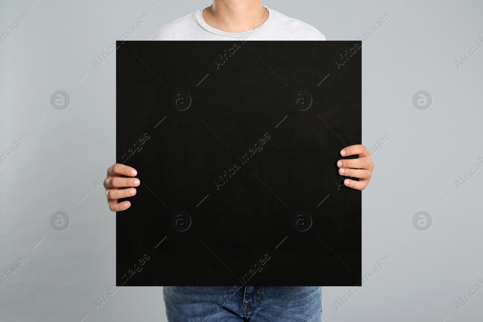 Photo of Man holding black blank poster on grey background, closeup. Mockup for design