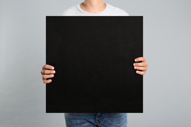 Man holding black blank poster on grey background, closeup. Mockup for design
