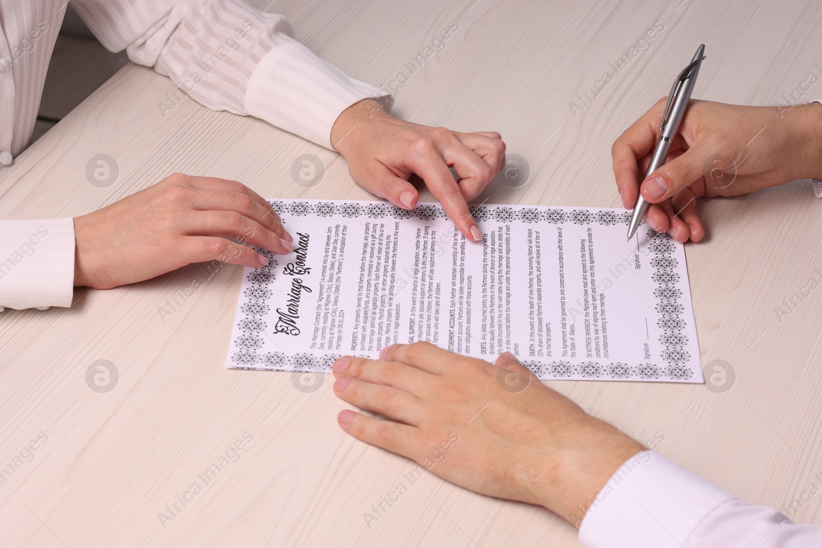 Photo of Man and woman signing marriage contract at light wooden table, closeup