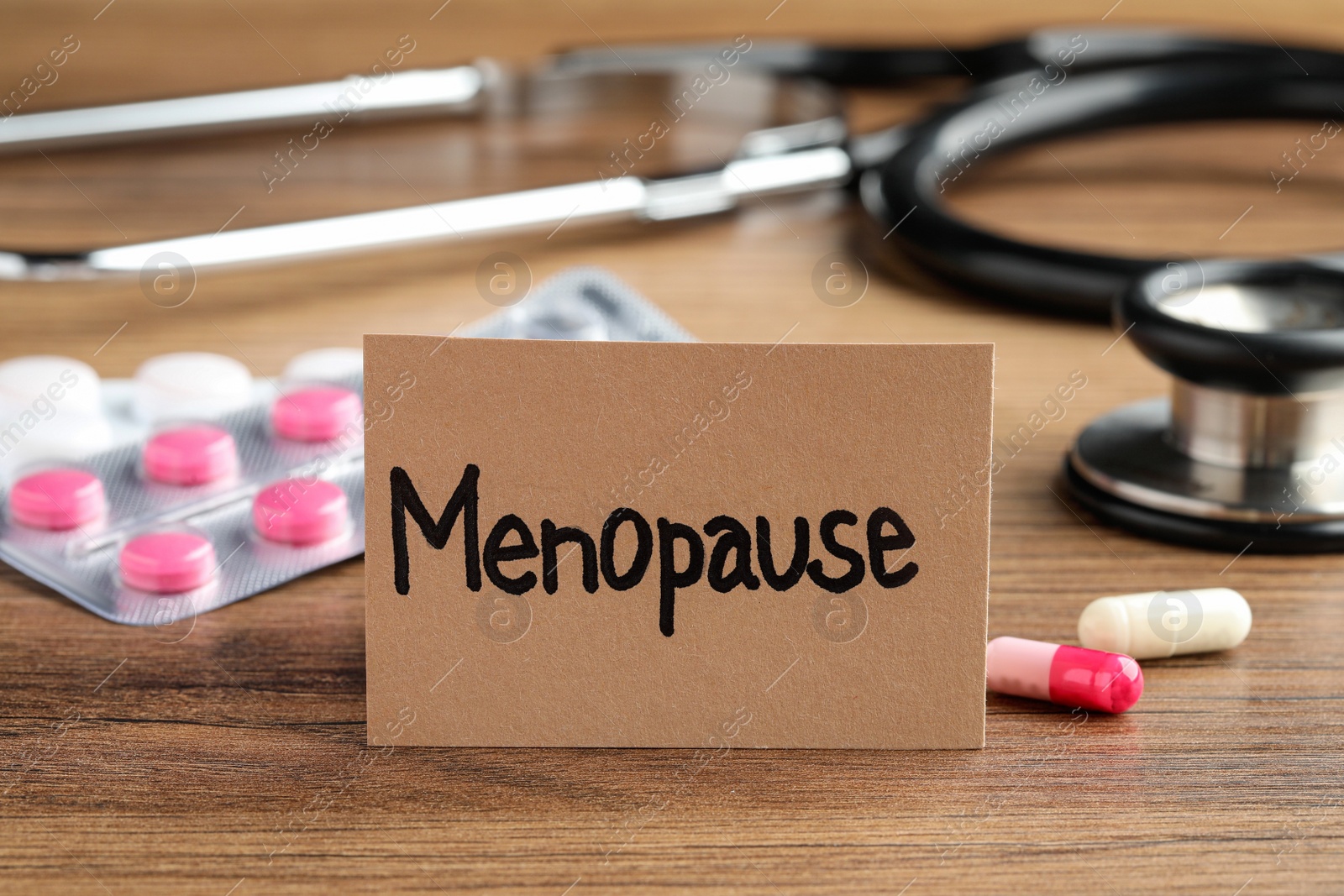 Photo of Card with word Menopause, pills and stethoscope on wooden table