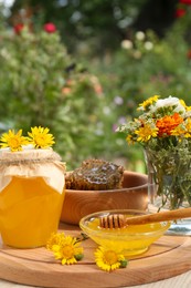 Delicious honey, combs and different flowers on wooden table in garden