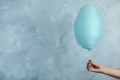 Woman holding sweet cotton candy on light blue background, closeup view. Space for text