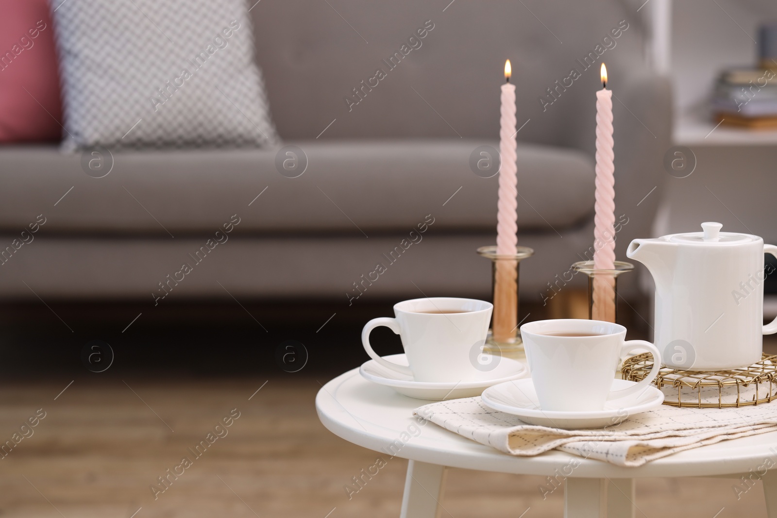 Photo of Cups of tea, teapot and burning candles on white coffee table indoors. Space for text