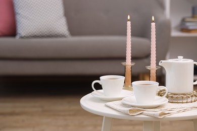 Cups of tea, teapot and burning candles on white coffee table indoors. Space for text