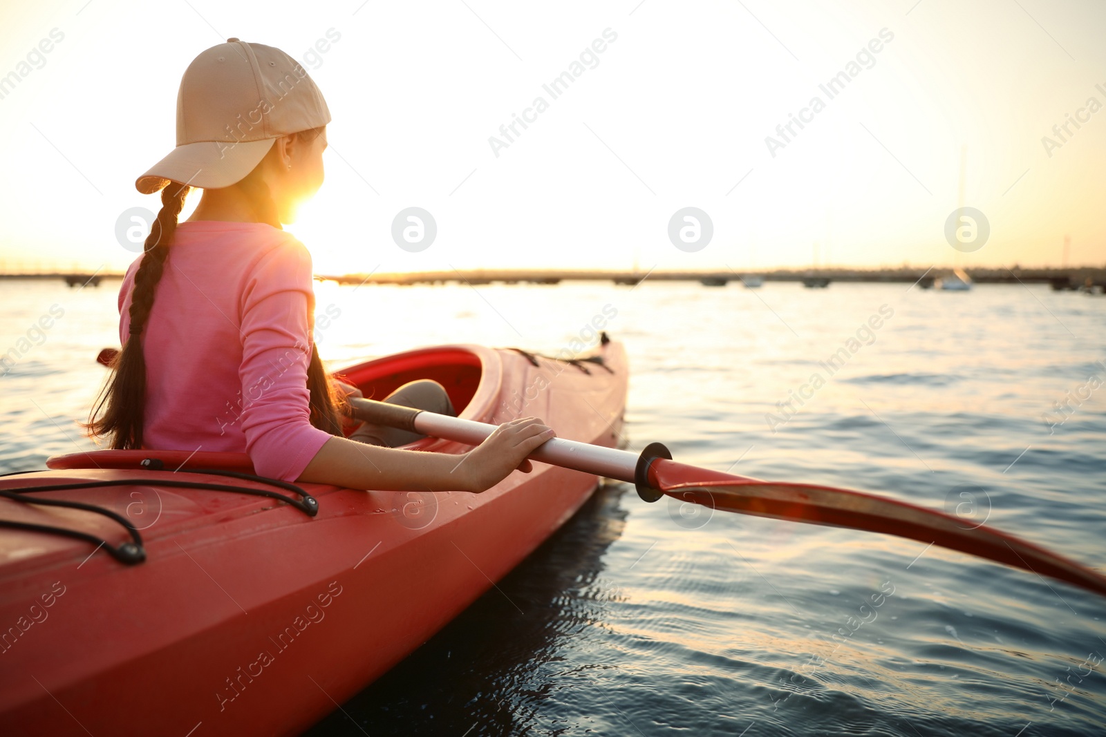 Photo of Little girl kayaking on river at sunset. Summer camp activity