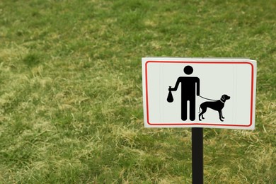 Sign board PLEASE CLEAN UP AFTER YOUR DOGS on green lawn