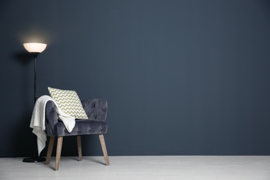 Photo of Stylish armchair with pillow and plaid near dark wall, space for text. Interior design