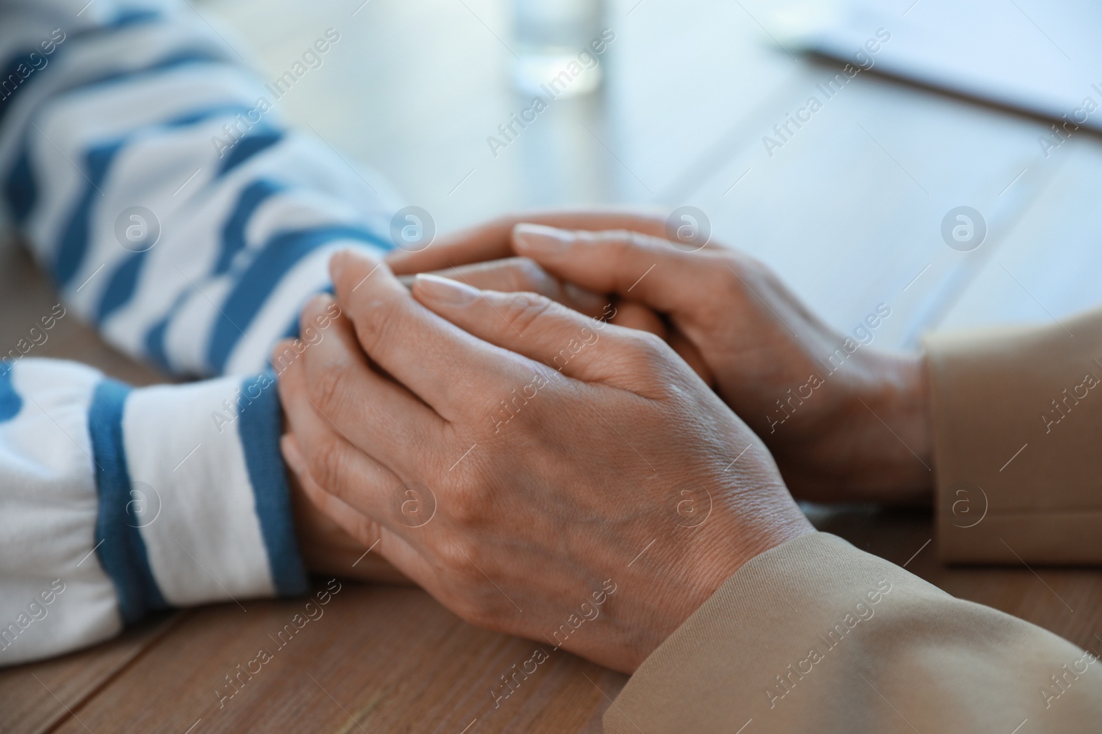 Photo of Psychotherapist holding patient's hands at table indoors, closeup