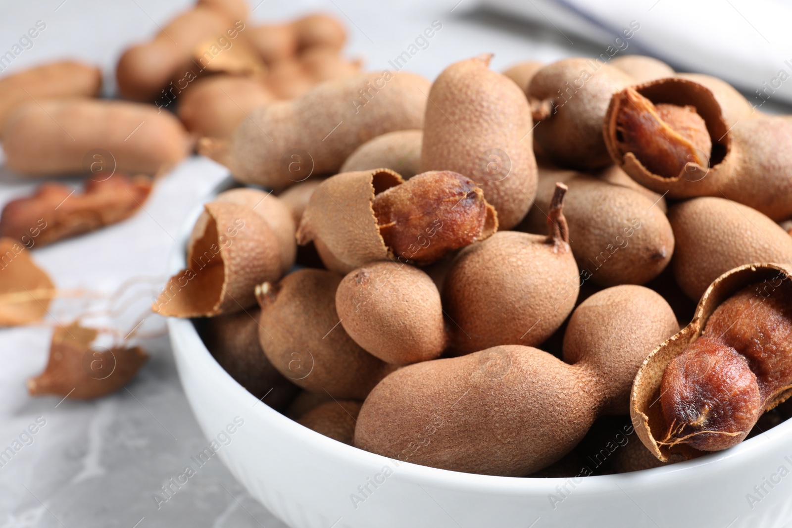 Photo of Delicious ripe tamarinds in ceramic bowl on table, closeup