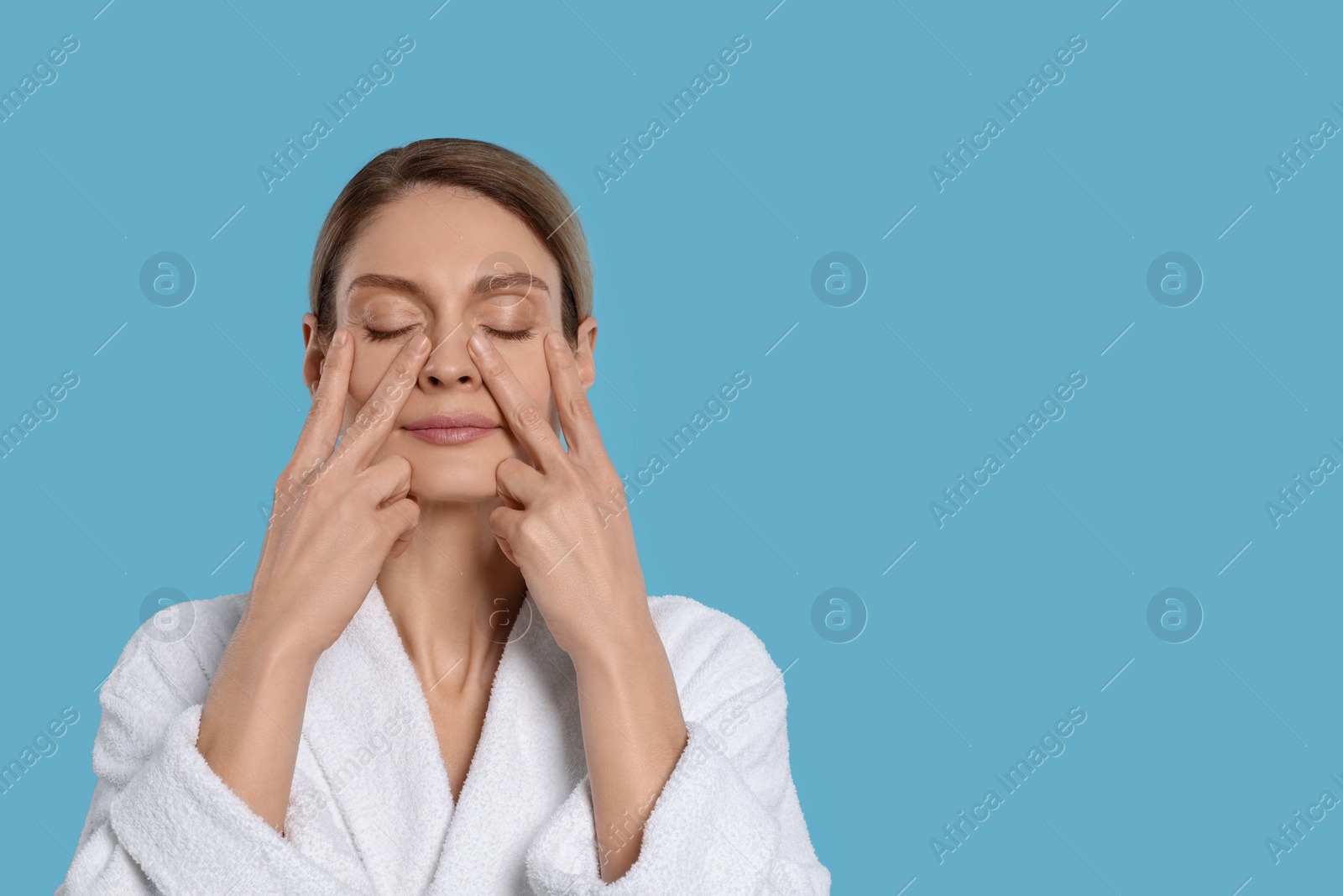 Photo of Woman massaging her face on turquoise background. Space for text