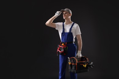 Photo of Professional repairman with tool box on black background. Space for text