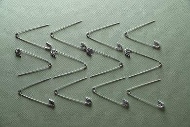 Many safety pins on green background, flat lay