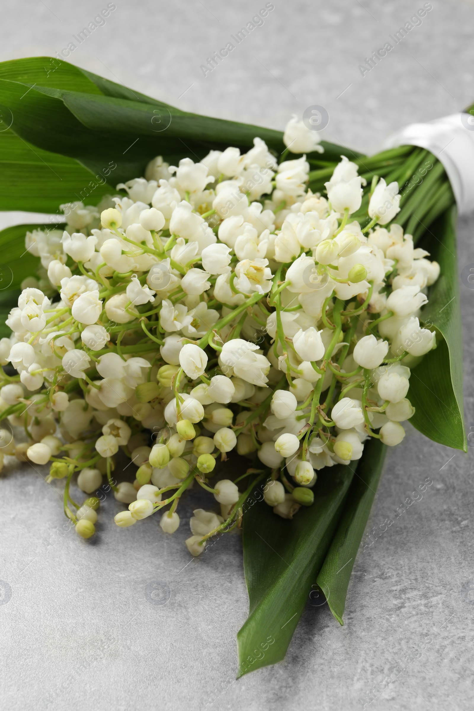 Photo of Beautiful lily of the valley bouquet on grey table, closeup