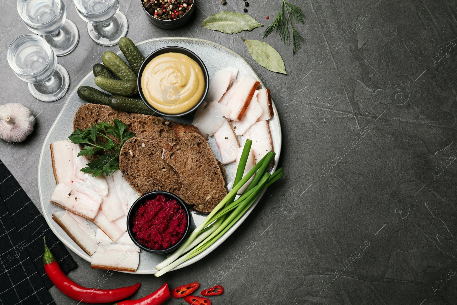 Photo of Tasty salt pork with rye bread and sauces served on grey table, flat lay. Space for text