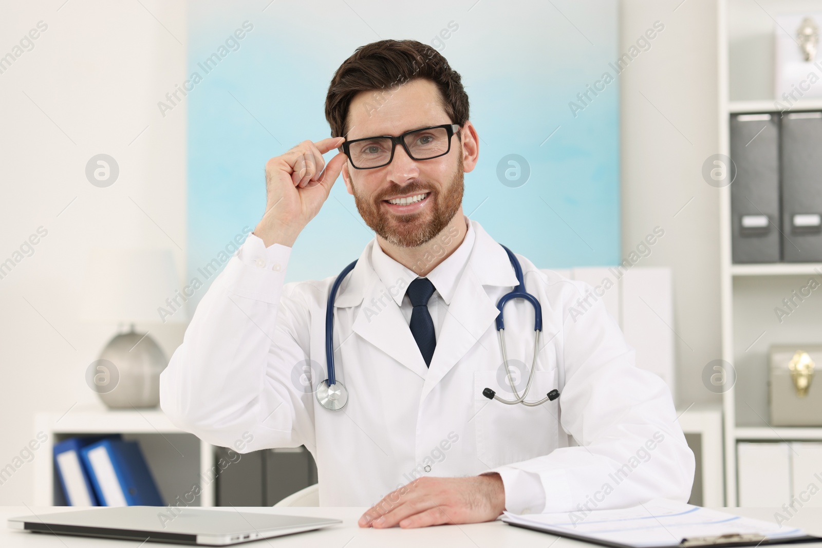 Photo of Medical consultant with glasses and stethoscope at table in clinic