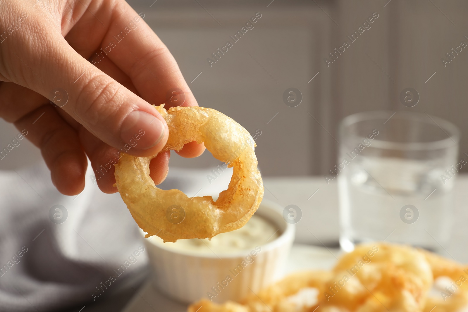 Photo of Woman holding homemade crispy onion ring over table, closeup