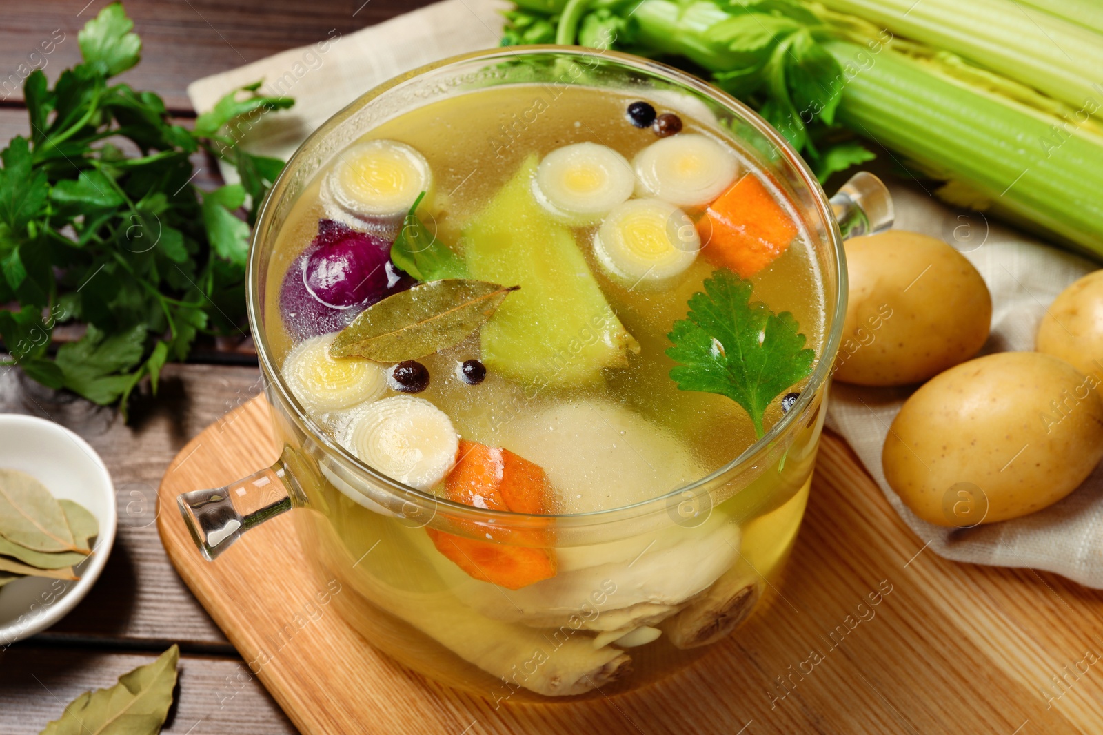 Photo of Glass pot with tasty bouillon and different ingredients on wooden table