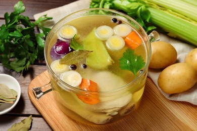 Glass pot with tasty bouillon and different ingredients on wooden table