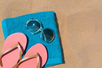 Photo of Folded soft blue beach towel with flip flops and sunglasses on sand, flat lay. Space for text
