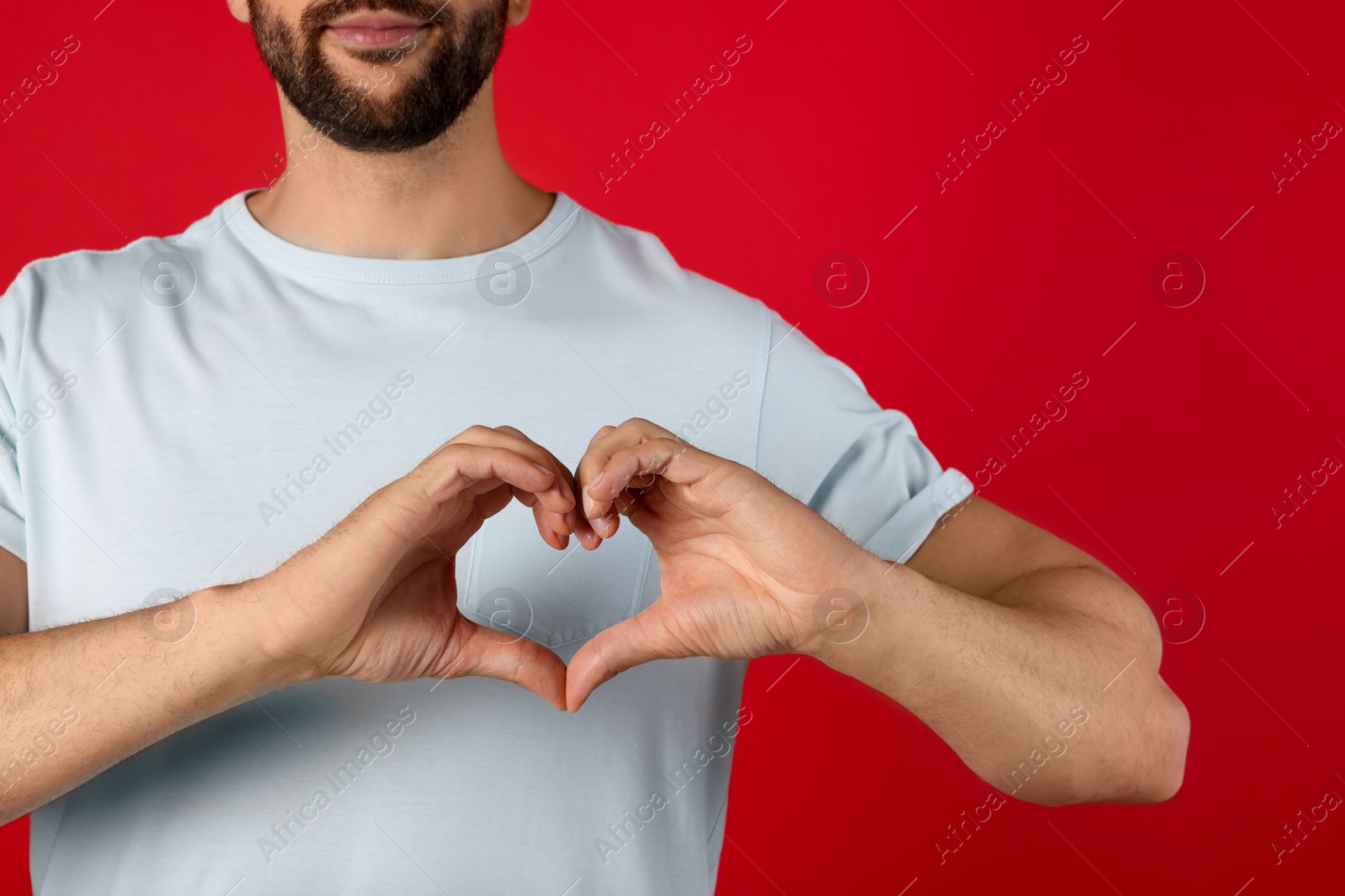 Photo of Man making heart with hands on red background, closeup