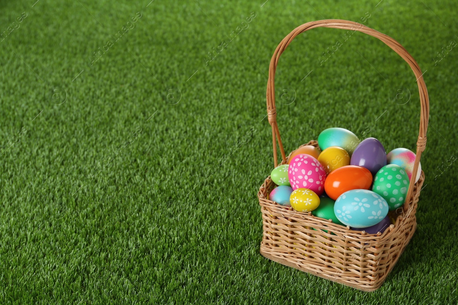 Photo of Wicker basket with Easter eggs on green grass. Space for text